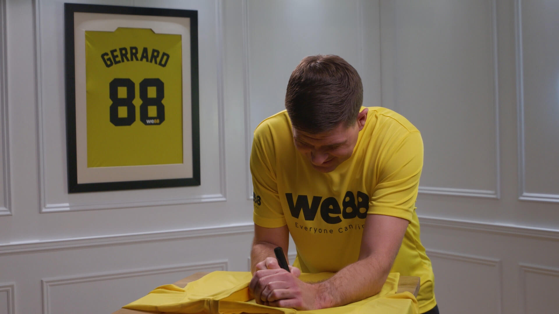 WE88 26/27 Global Brand Ambassador Steven Gerrard signing an official yellow jersey during an exclusive behind-the-scenes shoot