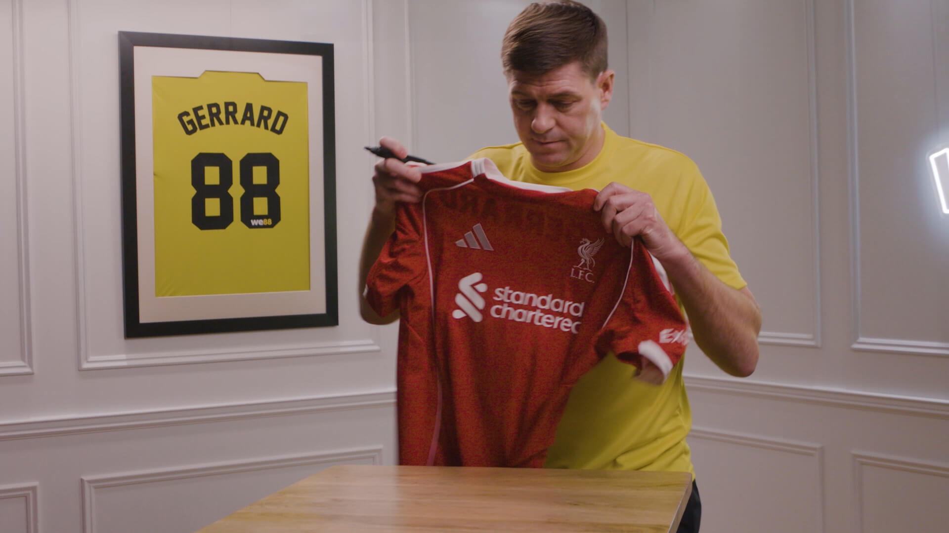 WE88 26/27 Global Brand Ambassador Steven Gerrard holding up a red Liverpool jersey to sign during a behind-the-scenes shoot