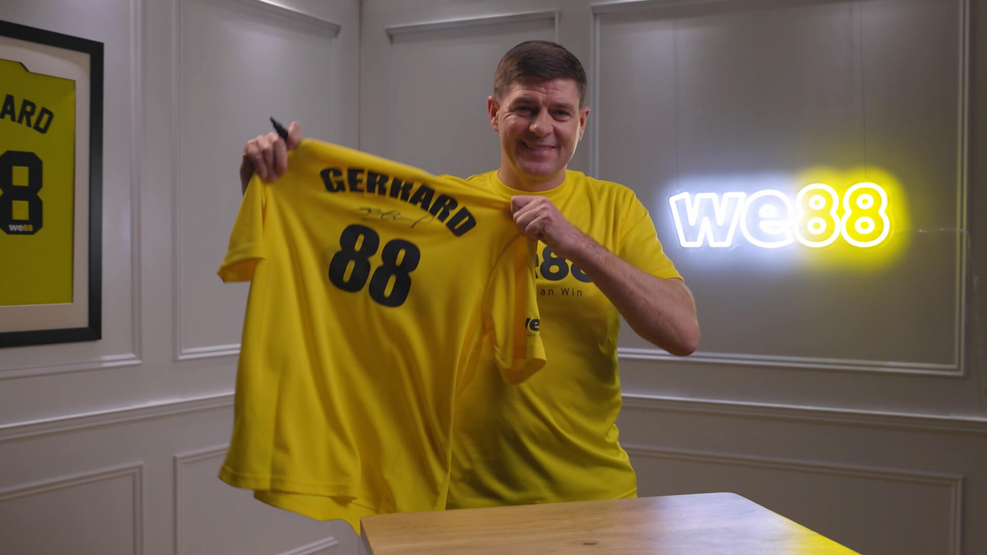 WE88 26/27 Global Brand Ambassador Steven Gerrard proudly holding up a signed yellow Gerrard 88 jersey