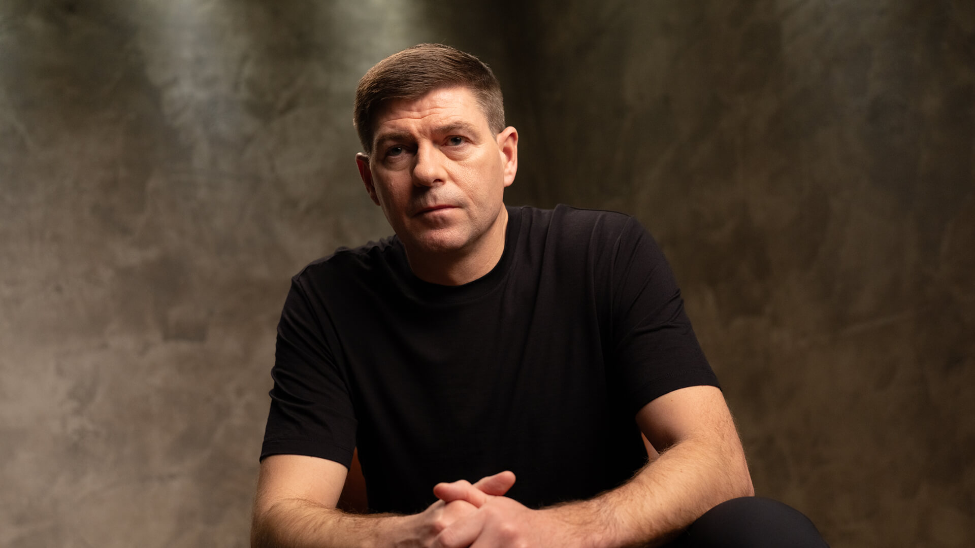 WE88 26/27 Global Brand Ambassador Steven Gerrard sitting with clasped hands in a serious studio portrait
