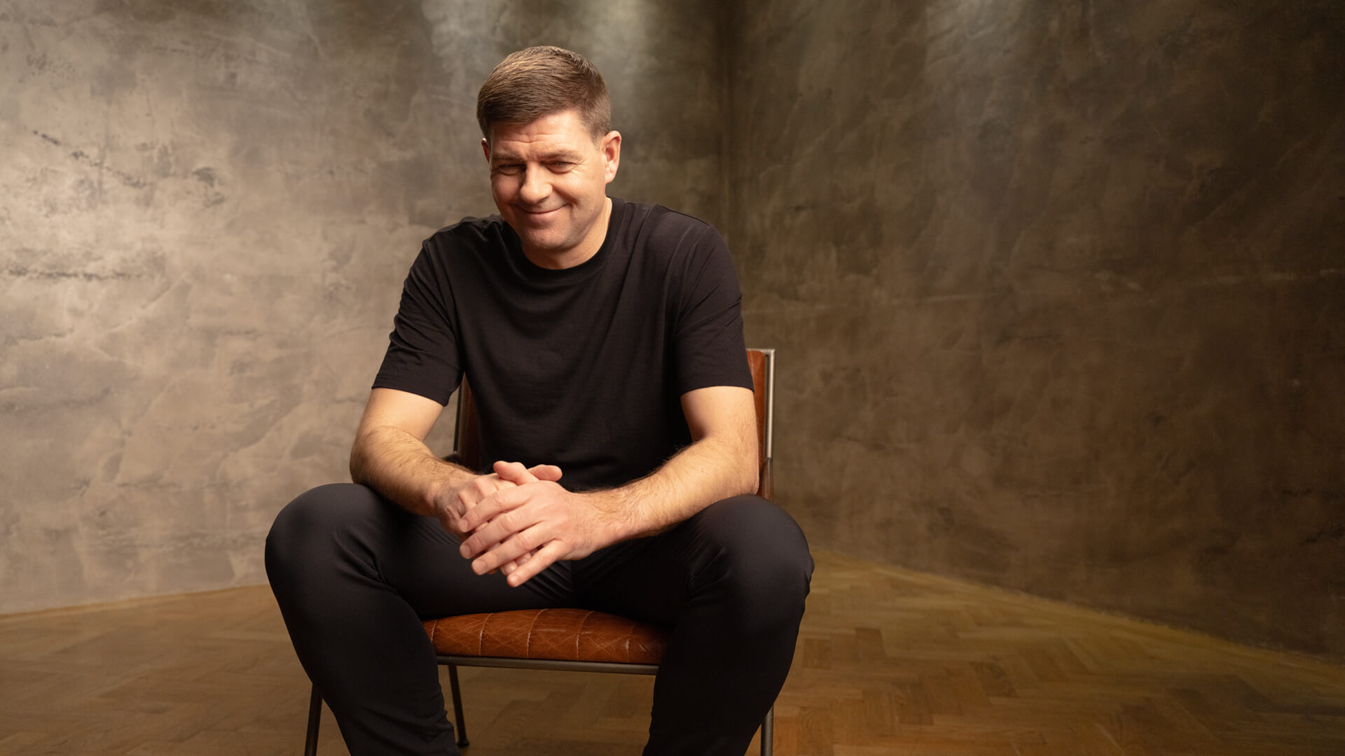 WE88 26/27 Global Brand Ambassador Steven Gerrard sharing a relaxed smile while seated during a behind-the-scenes studio shoot